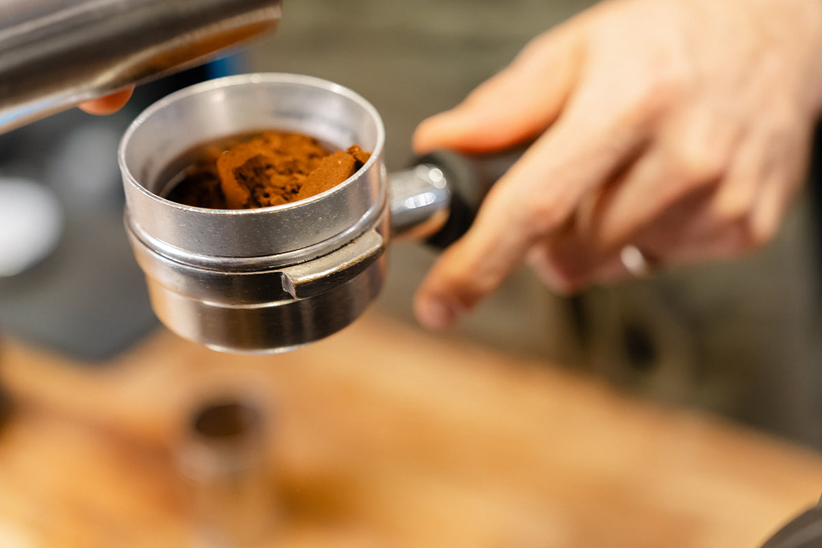 Close-up of loose espresso grounds in a portafilter fitted with a dosing funnel, ready for distribution.