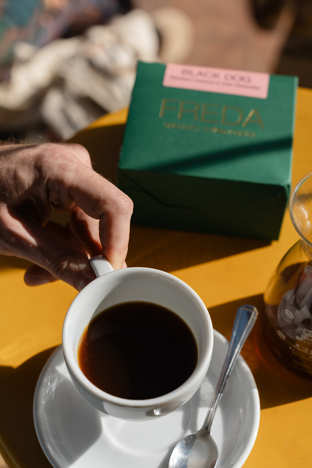 Hand holding coffee cup with freda-coffee.live packaging in background, taken in Bond Street Coffee, Brighton Best Cafe, Sussex
