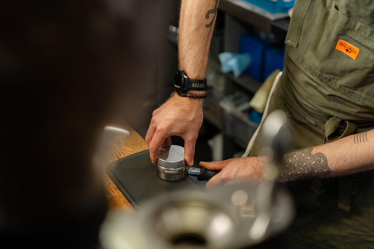 Barista pressing a PUSH tamper into a portafilter supported on a tamping mat.